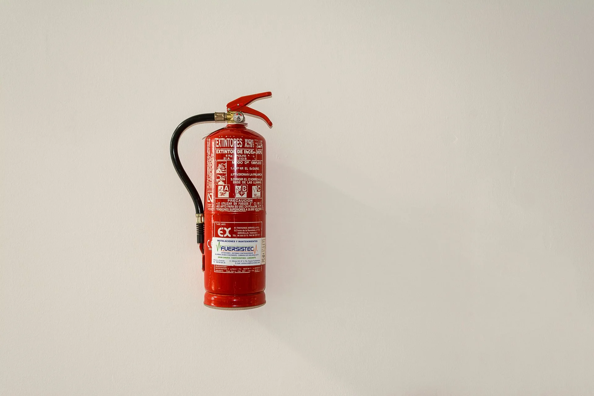 Extintor vermelho instalado em uma parede clara.