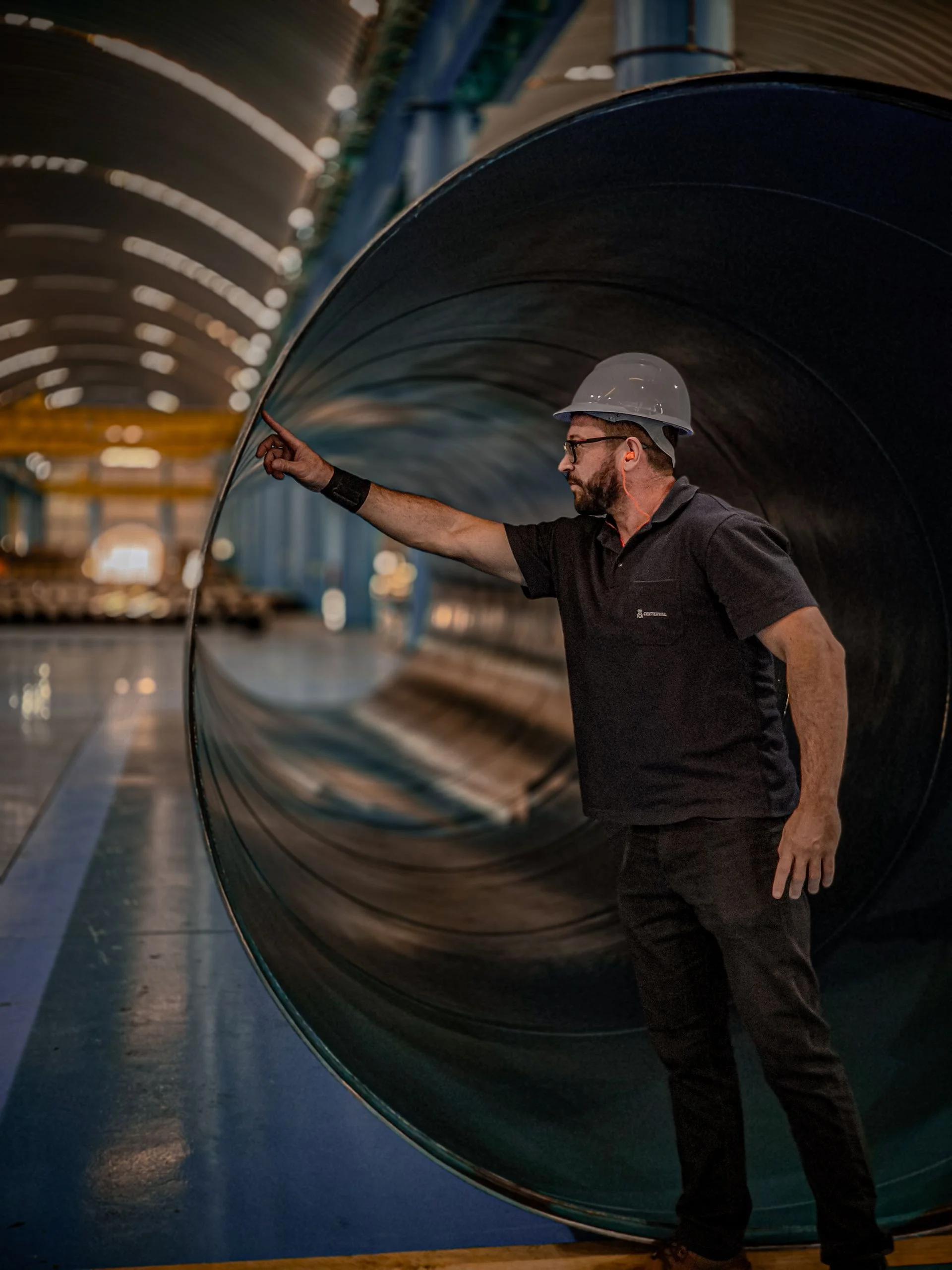 Profissional com capacete observa uma tubulação em instalação industrial.