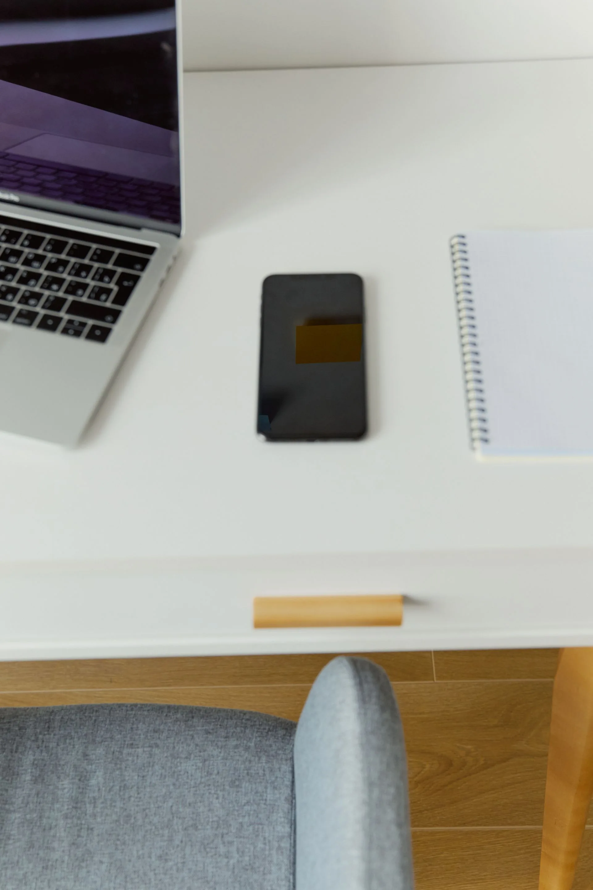 Mesa organizada com celular, computador e caderno.