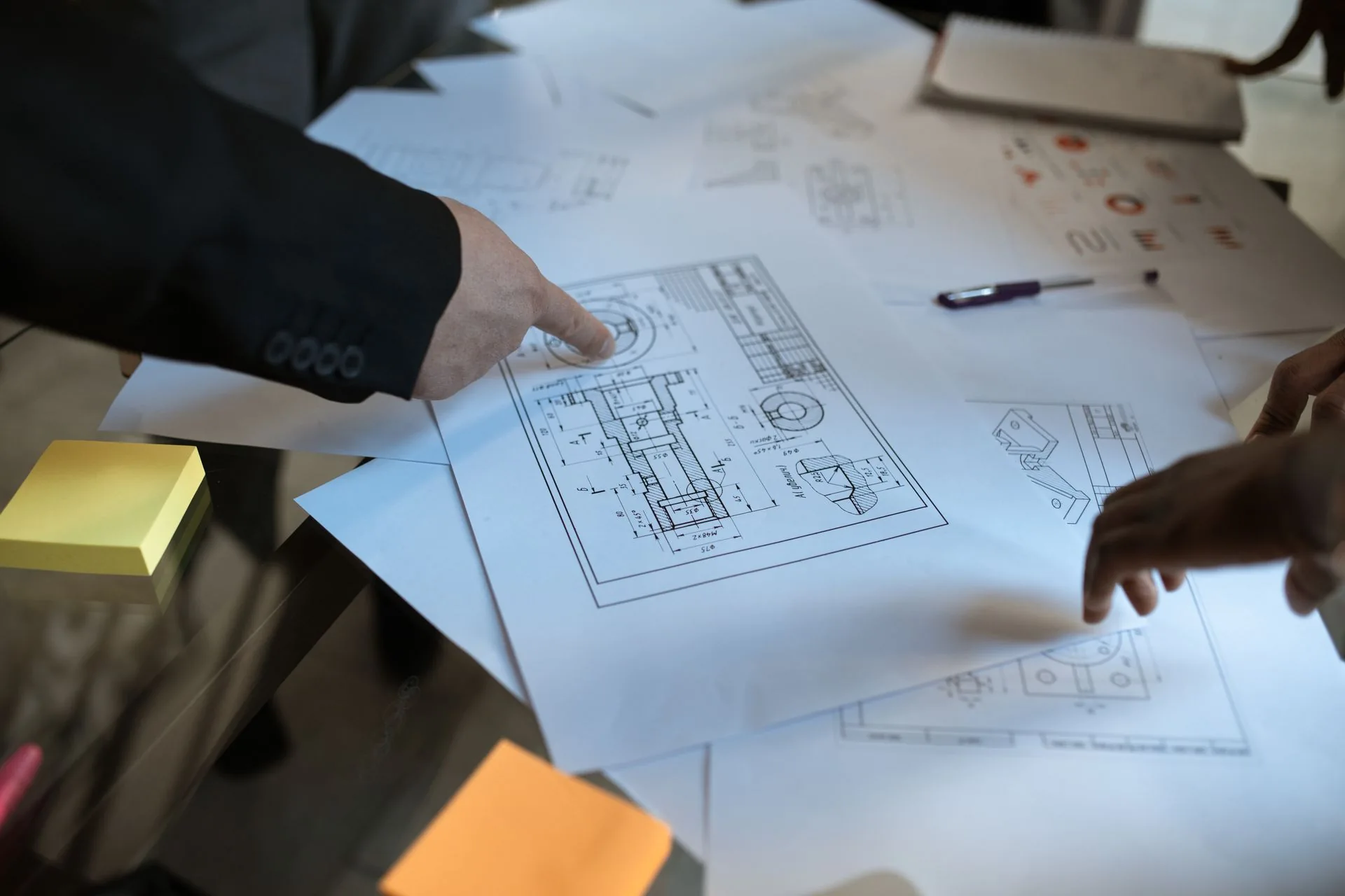 Mãos apontam detalhes de uma planta técnica sobre a mesa.