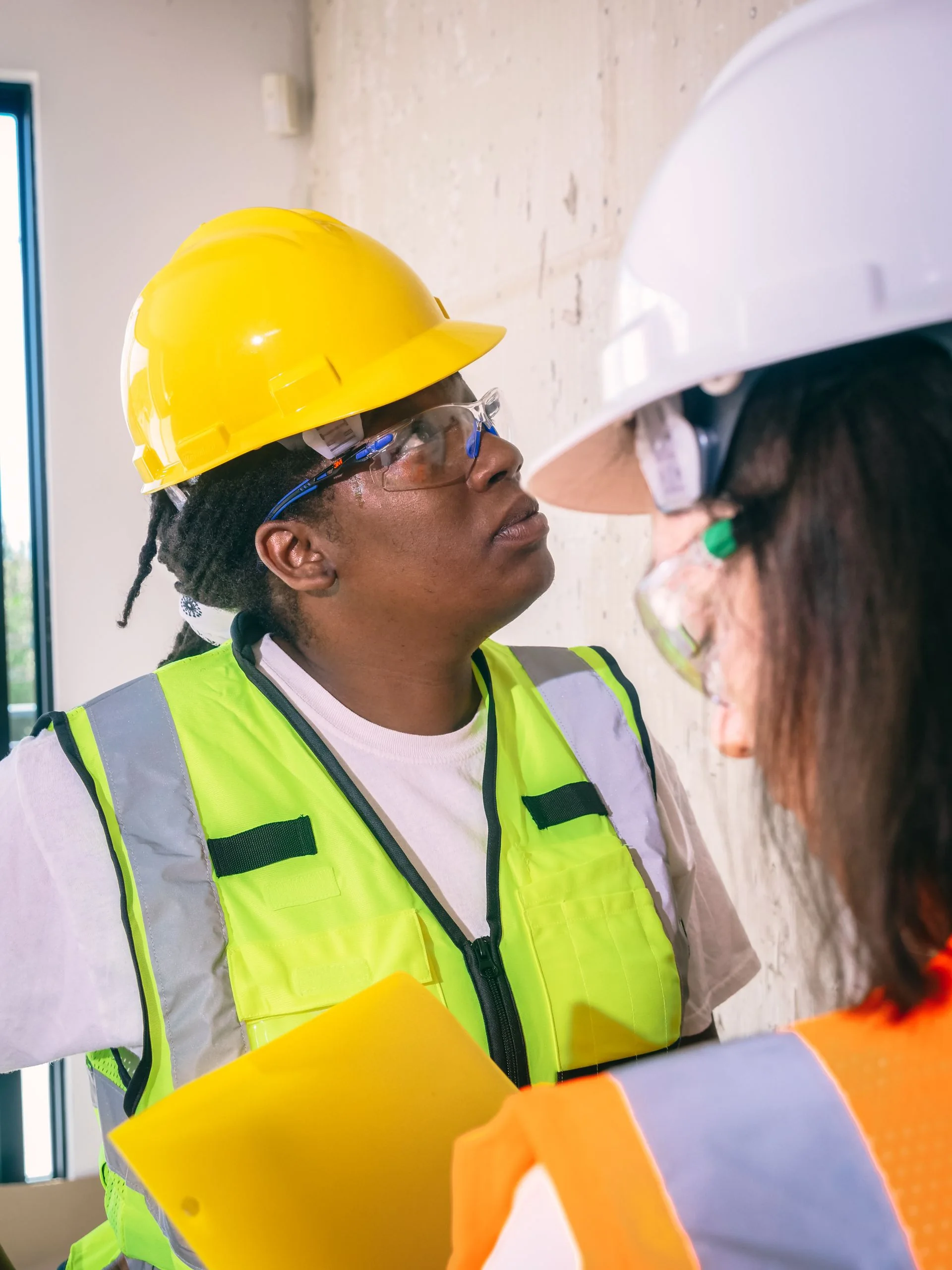 Profissionais com capacetes, óculos e coletes observam um ambiente em construção.